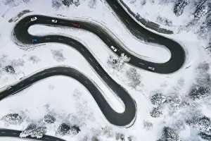 Aerial view of cars driving on narrow bends of mountain road in the snow Aerial view of cars driving on narrow bends of mountain road in the snow