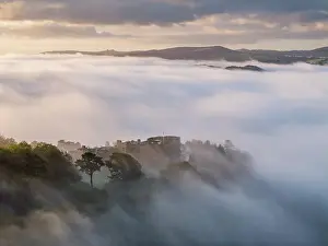 Aerial view of Castle Drogo emerging from a sea of morning mist, Dartmoor National Park, Devon, England. Autumn (October) 2023