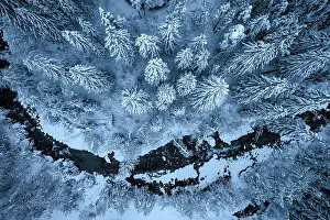 Rime Ice Prints: Aerial view of an icy river flowing along a winter snowy forest at dusk