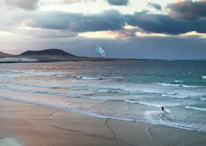 Kitesurfing Prints: Aerial view of a man kitesurfing at Famara beach with Caleta de Famara in background