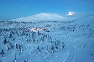 Ski Resort Prints: Aerial view of a snowy mountain road in the frozen forest nearby a ski area at dusk