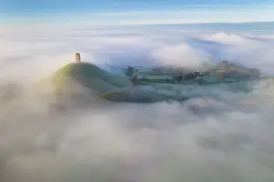 Aerial view of St Michael's Tower on Glastonbury Tor at dawn on a misty morning, Glastonbury, Somerset, England. Autumn (November) 2022