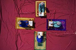 Holy Gallery: Aerial view of four student reading the koran in circle sitting on colourful carpet in
