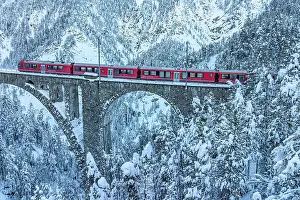 Railway Track Prints: Aerial view of the Swiss red train traveling on Wiesen viaduct across snowy frozen woods