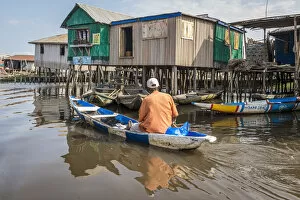 Africa, Benin, Ganvie. A man in his canoe passing by a shop in the floating village