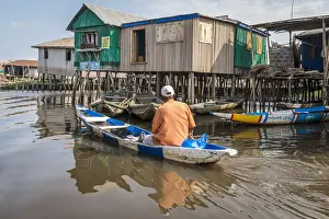 Ganvie Prints: Africa, Benin, Ganvie. A man in his canoe passing by a shop in the floating village