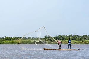 Africa, Benin, Mono Department. Fishermen in a traditional canoe casting a net