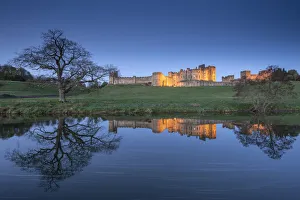 Alnwick Castle illuminated at twilight and reflected in the River Aln, Northumberland Alnwick Castle illuminated at twilight and reflected in the River Aln, Northumberland