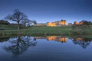 Northumberland Prints: Alnwick Castle illuminated at twilight and reflected in the River Aln, Northumberland
