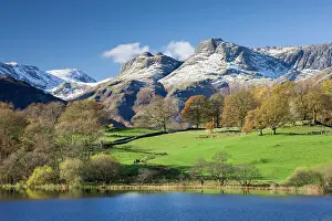 Autumn colours beside Loughrigg Tarn with views to the snow dusted mountains of the Langdale Pikes