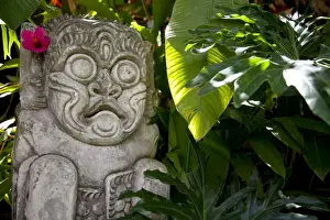 Lesser Sunda Islands Prints: Bali, Ubud. A stone carving, adorned with a hibiscus flower, sits in tropical gardens
