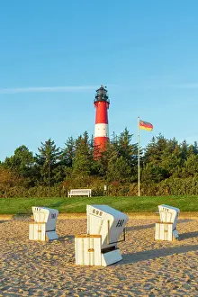 Beach chairs near German flag and Hornum lighthouse in background at sunrise, Hornum beach, Sylt, Nordfriesland, Schleswig-Holstein, Germany