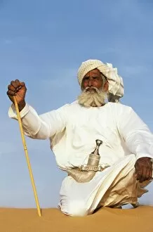 A Bedouin man kneels on top of a sand dune in the desert