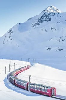 Bernina Express red train passing Lago Bianco in a scenic winter mountain landscape