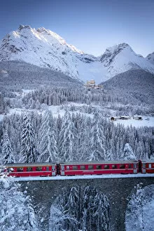 Bernina Express train on viaduct surrounding Tarasp Castle and snow capped mountains
