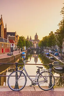 Urban Landscape Prints: A bike on a bridge with St. Nicholas church in the background at sunrise in Amsterdam