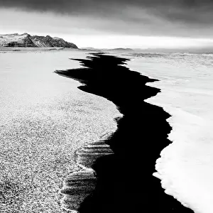 Black sand beach fringed by snow and surf, near Jokulsarlon, South Iceland