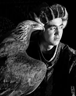 Mongolia Prints: Black & white portrait of a young Kazakh Eagle Hunter posing with his trained golden eagle