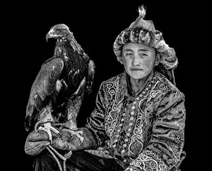 Mongolia Prints: Black & white portrait of a young Kazakh Eagle Hunter posing with his trained golden eagle