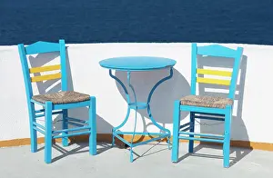 Aegean Prints: Blue chairs and table against white wall and sea