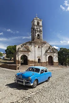 Valle De Los Ingenios Prints: Blue classic car passes old church, Trinidad, Sancti Spiritus Province, Cuba