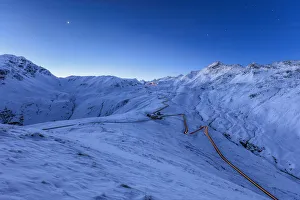 Blue light of dusk on the snowy landscape and the hairpin turns of Stelvio Pass Braulio Blue light of dusk on the snowy landscape and the hairpin turns of Stelvio Pass Braulio