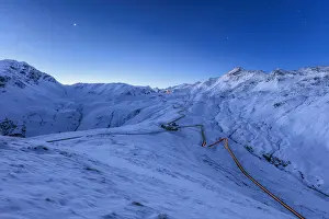 Mountain Pass Prints: Blue light of dusk on the snowy landscape and the hairpin turns of Stelvio Pass Braulio