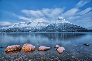 Blue sky at dusk and snowy peaks are reflected in the frozen sea at Oteren Storfjorden Lapland Lyngen Alps Tromsa¸ Norway Europe