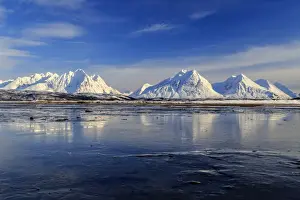 The blue sky and snow capped mountains are reflected in the frozen water Breivikeidet Lyngen Alps Tromsa¸ Lapland Norway Europe