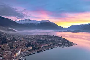 Sunlight Prints: Burning sky at dawn over the snowcapped mountains and Domaso old town, aerial view