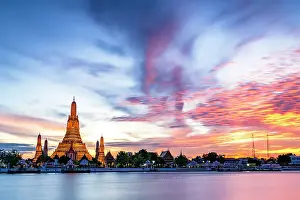Building Exterior Prints: Burning sky at sunset over the iconic Wat Arun Buddhist temple reflected in Chao Phraya River