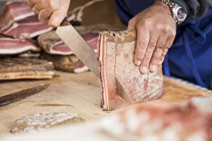 a butcher is cutting a piece of Speck, the typical kind of prosciutto, bolzano