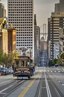 Cable car crossing California Street with Bay Bridge backdrop, San Francisco, California, USA