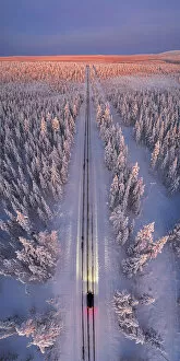 Finnish Gallery: a car with headlight on travelling empty road at dawn, Pallas-Yllastunturi National Park, Muonio