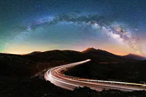 Traffic Prints: Car trails lights on empty desert road under the arched Milky Way
