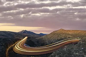 Motion Gallery: Car trails lights on road crossing the desert landscape at sunrise, Fuerteventura