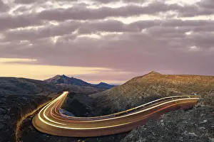 Road Trip Prints: Car trails lights on road crossing the desert landscape at sunrise, Fuerteventura