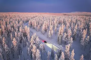 Road Trip Prints: Car traveling on icy road crossing the winter forest covered with snow from above