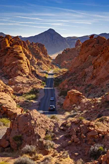 Cars driving on a straight road between red rocks during sunny day Cars driving on a straight road between red rocks during sunny day