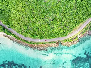 West Indies Prints: Cars traveling on a coastal road in between the crystal Caribbean sea and lush plants