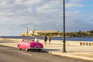 Habana Prints: Classic car driving along the Malecon with Castillo De Los Tres Reyes Del Morro