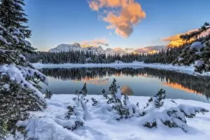 The colors of dawn on the snowy peaks and woods reflected in PalA AA┬╣ Lake Malenco