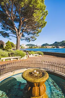 Reading Prints: Como, Lombardy, Italy. A fountain on the lake front and a woman reading on a bench