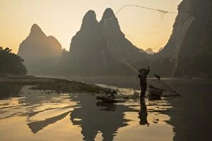 Guangxi Province Gallery: Cormorant fisherman throwing net on Li River at dawn, Xingping, Yangshuo, Guangxi, China