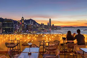 Sitting Prints: Couple at SipSip Rooftop Bar and skyline of Hong Kong Island at sunset, Hong Kong, China