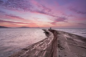 Lyme Bay Prints: Couple standing on The Cobb at sunrise, Lyme Regis, Dorset, England