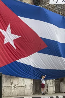 Images Dated 25th April 2017: Cuba, Boy saluting to Huge Cuban flag hanging across buildings in a street in Santa Clara