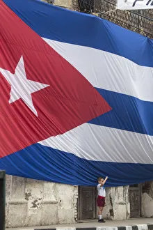Cuba, Boy saluting to Huge Cuban flag hanging across buildings in a street in Santa Clara Cuba, Boy saluting to Huge Cuban flag hanging across buildings in a street in Santa Clara