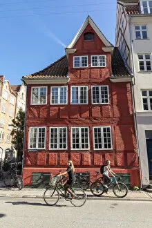 Images Dated 16th December 2021: Cyclists pass an old red house in Central Copenhagen, Copenhagen, Denmark