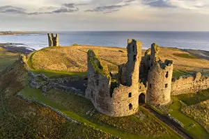 Northumberland Prints: Dunstanburgh Castles great gatehouse and Lilburn Tower illuminated in early morning
